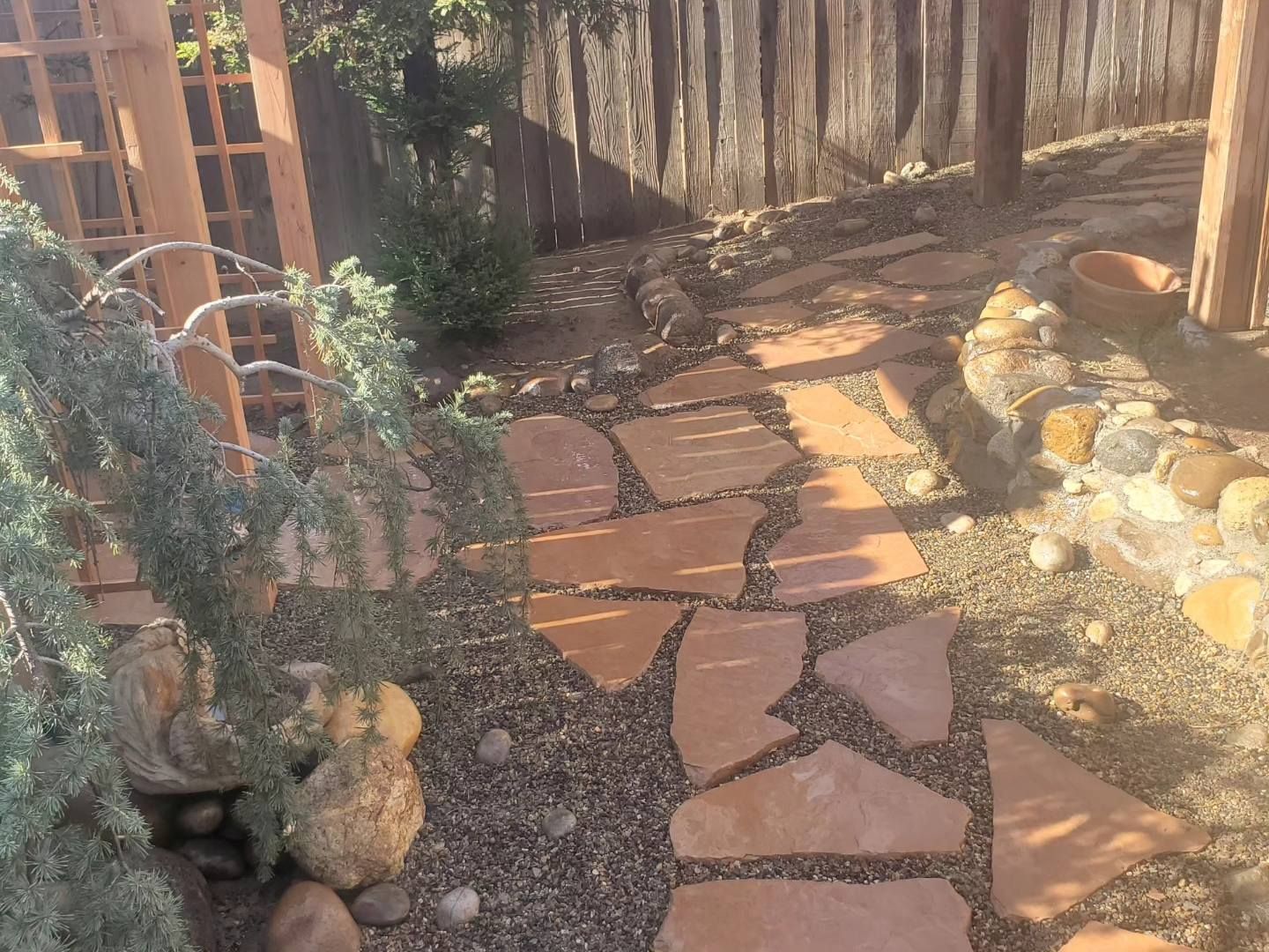 A stone walkway leading to a wooden pergola in a backyard.