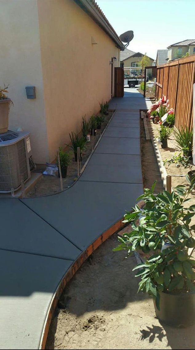 A sidewalk leading to a house with potted plants on the side of it.