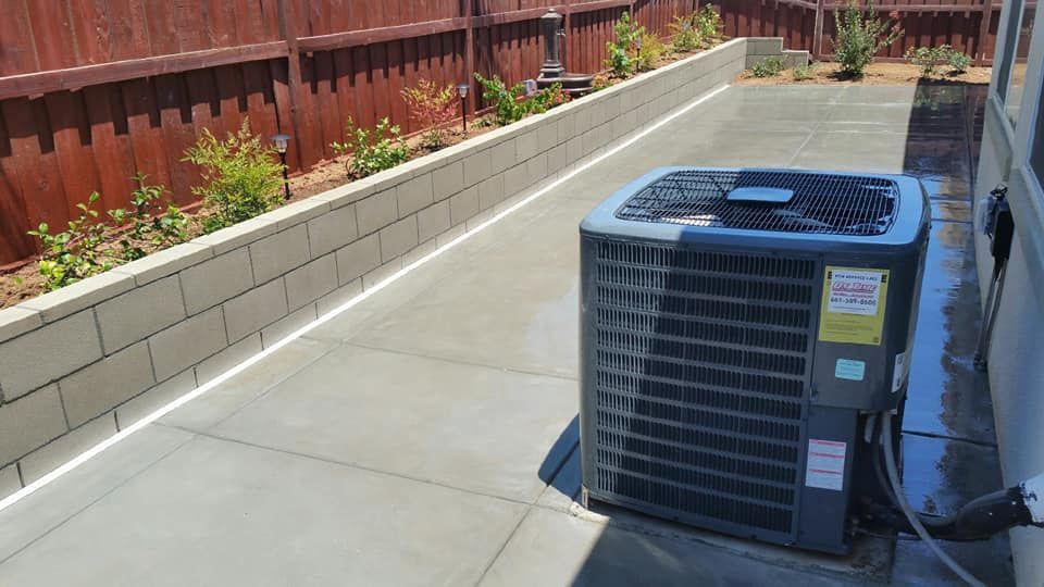 An air conditioner is sitting on the sidewalk next to a fence.