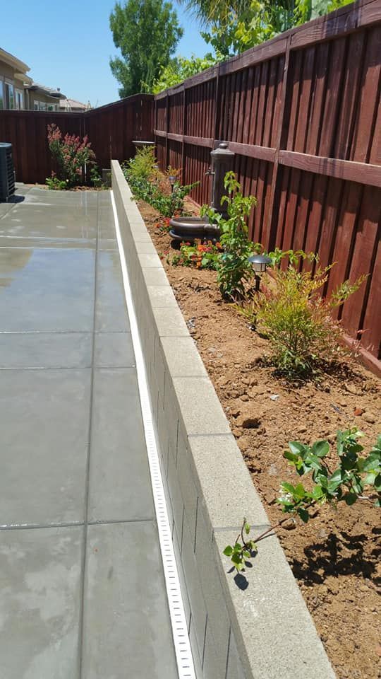 A concrete walkway leading to a garden with a wooden fence in the background.