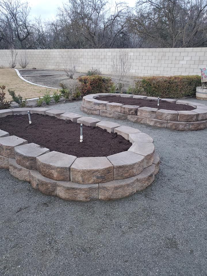 A couple of stone planters in a backyard with a brick wall in the background.