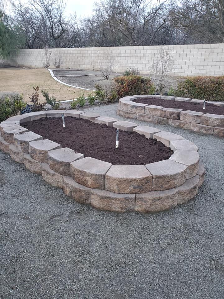 A stone planter filled with dirt and plants in a backyard.