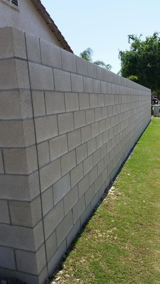 A large brick wall is sitting in the grass next to a house.