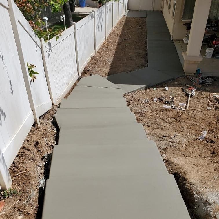 A concrete walkway is being built next to a white fence.