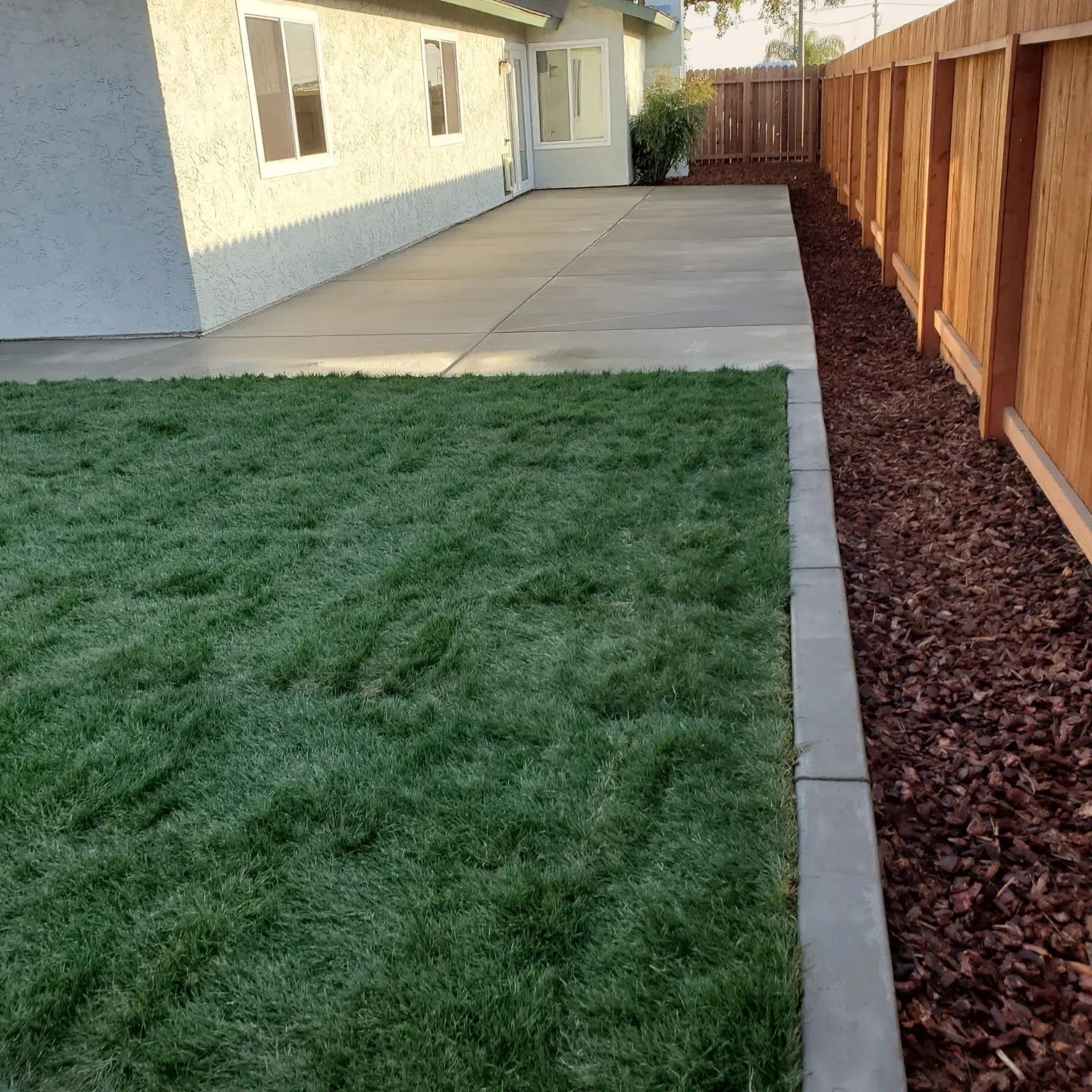 A backyard with a wooden fence and a concrete walkway