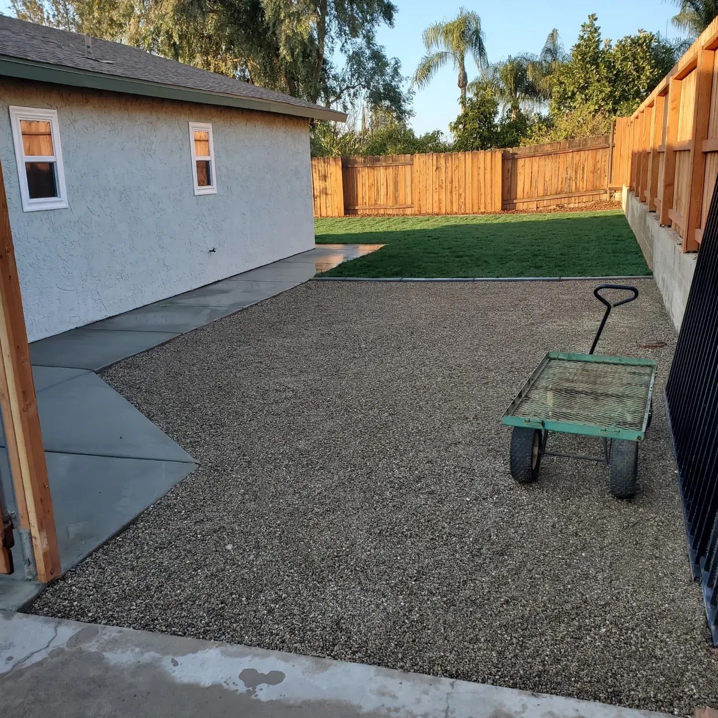 A wheelbarrow is sitting in a gravel yard in front of a house