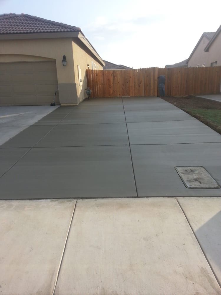 A concrete driveway in front of a house with a wooden fence