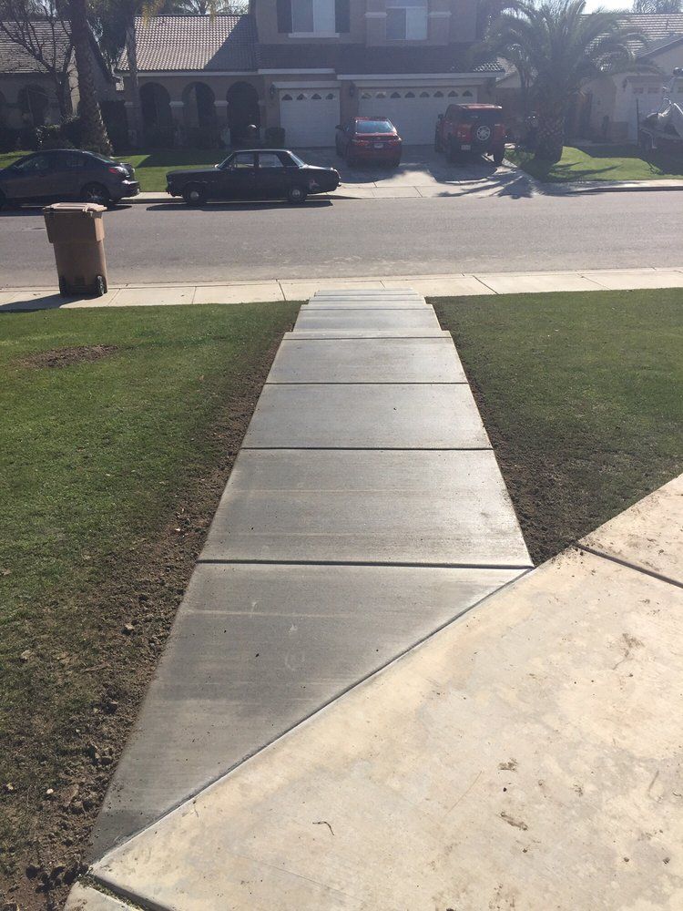 A concrete walkway leading to a house with a car parked on the side of the road.