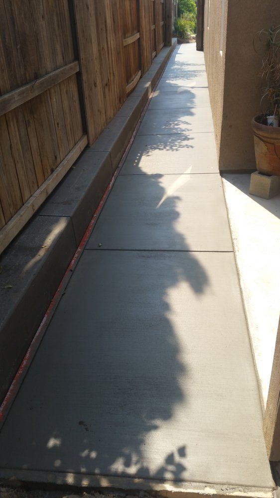 A concrete walkway with a wooden fence in the background.