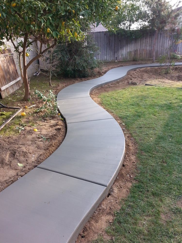 A curved concrete walkway leading to a fence in a backyard.