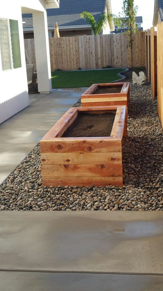 A row of wooden planters are sitting on top of gravel in a backyard.