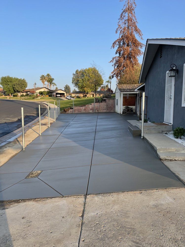 A concrete driveway leading to a house with a tree in the background.
