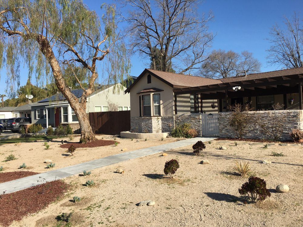 A house in the middle of a desert with a tree in front of it.
