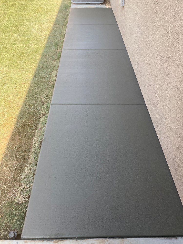 A concrete walkway leading to a house next to a grassy field.