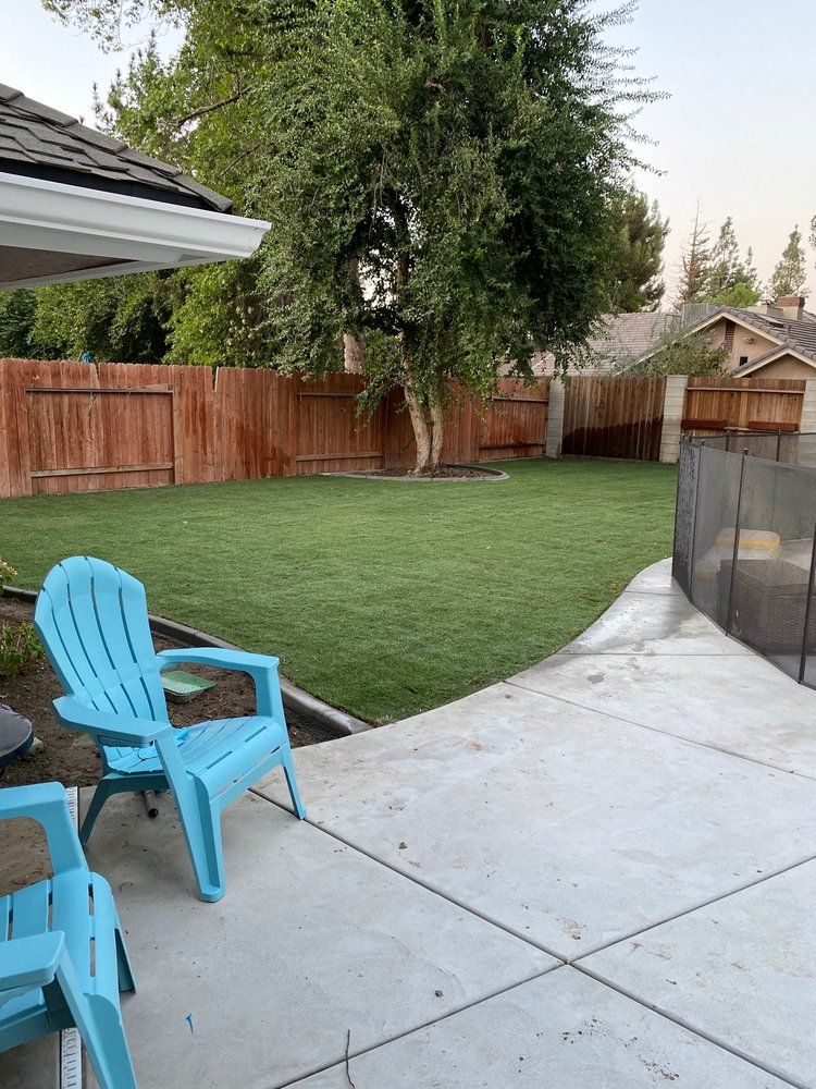 A patio with two blue chairs and a fence in the backyard.