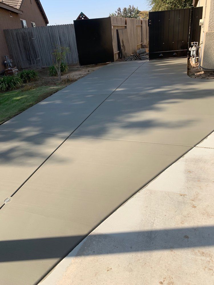 A concrete driveway with a fence in the background and a house in the background.
