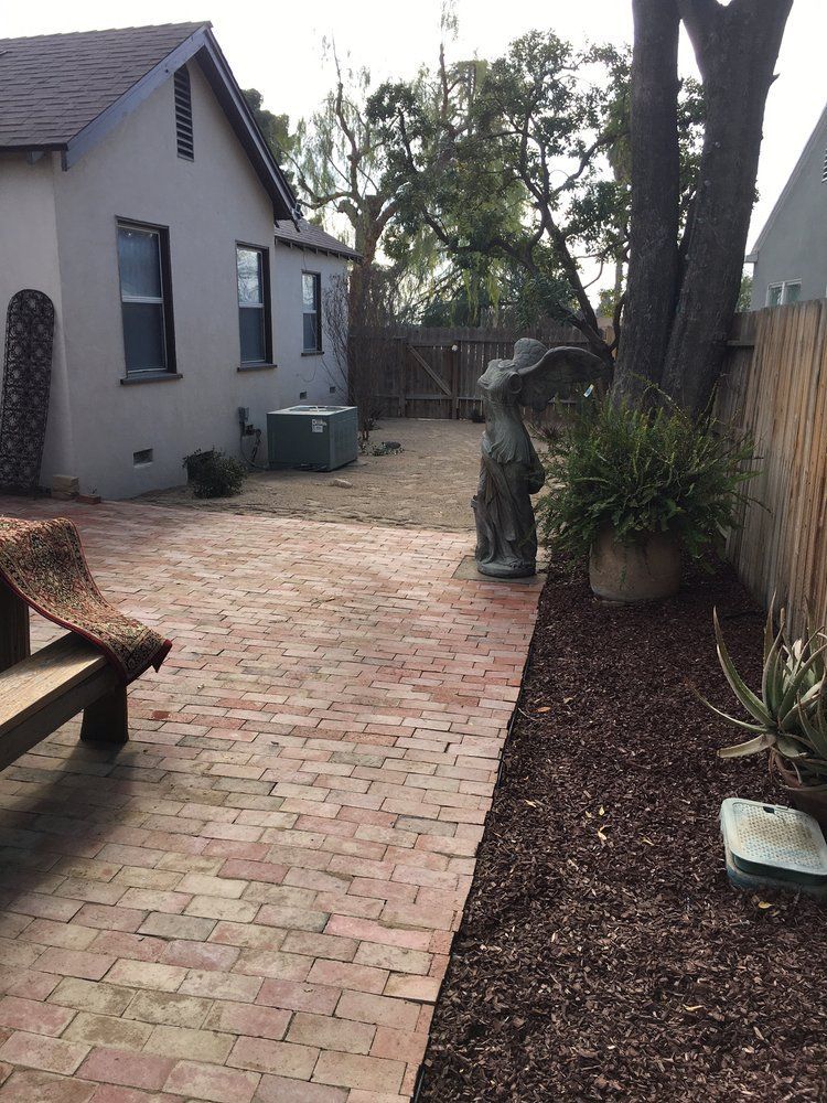 A brick walkway leading to a house with a statue of a man in a hat.