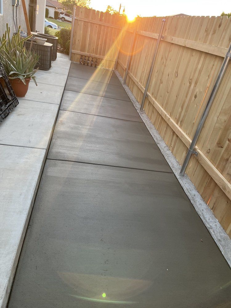 A concrete walkway leading to a wooden fence with the sun shining through it.