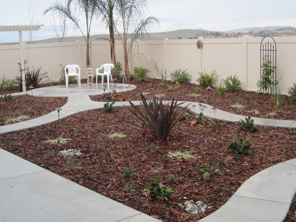 A garden with a concrete walkway and two white chairs