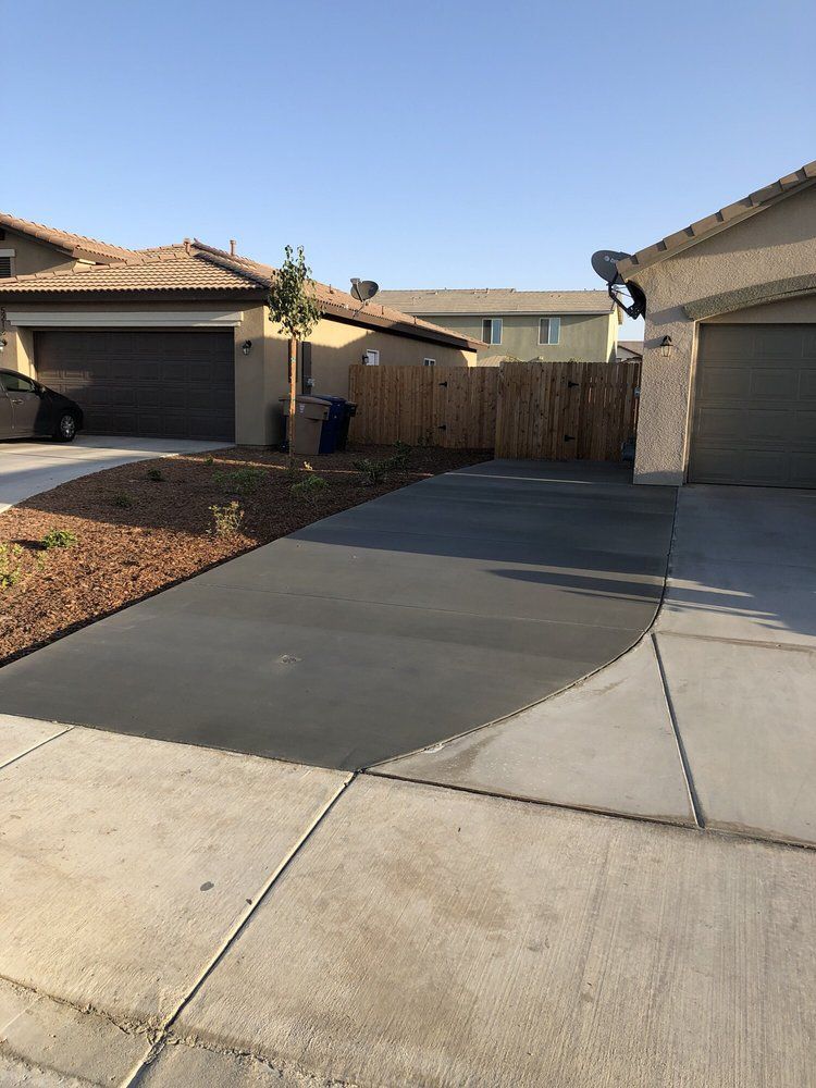 A concrete driveway leading to a house with a wooden fence.
