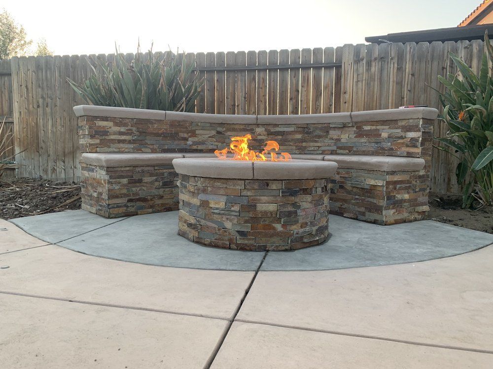 A fire pit is sitting on a patio next to a wooden fence.