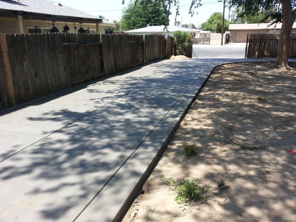A concrete driveway with a wooden fence in the background
