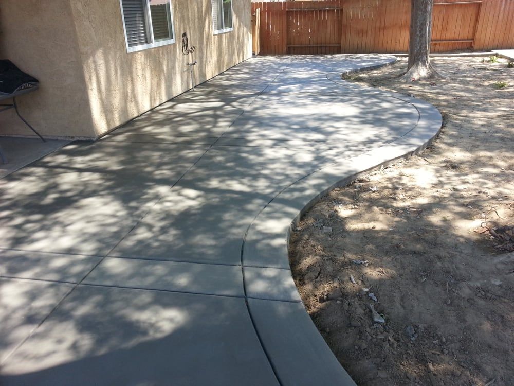 A concrete walkway leading to a house with a wooden fence in the background