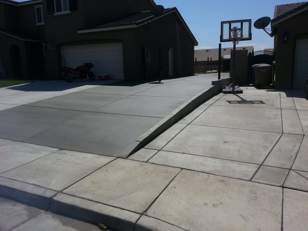 A concrete driveway with a basketball hoop in front of a house