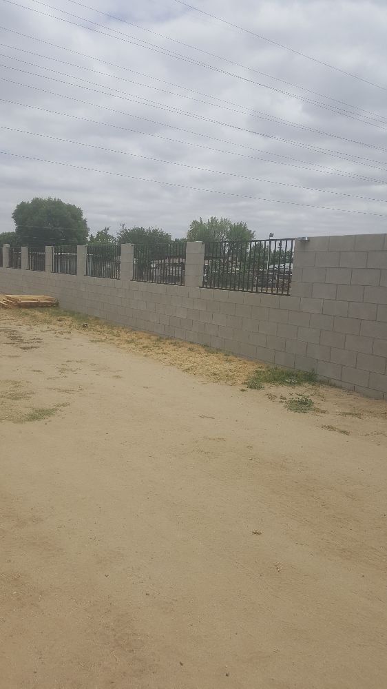 A brick wall surrounding a dirt road with trees in the background.