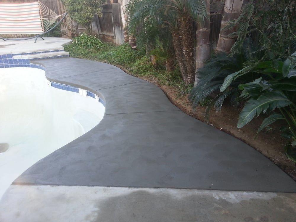 A concrete walkway leading to a swimming pool in a backyard.