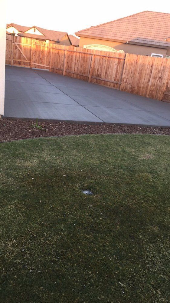 A concrete driveway with a wooden fence and a house in the background.