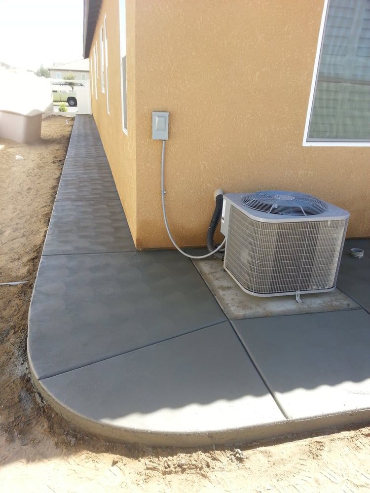 A concrete walkway with an air conditioner on the side of a house