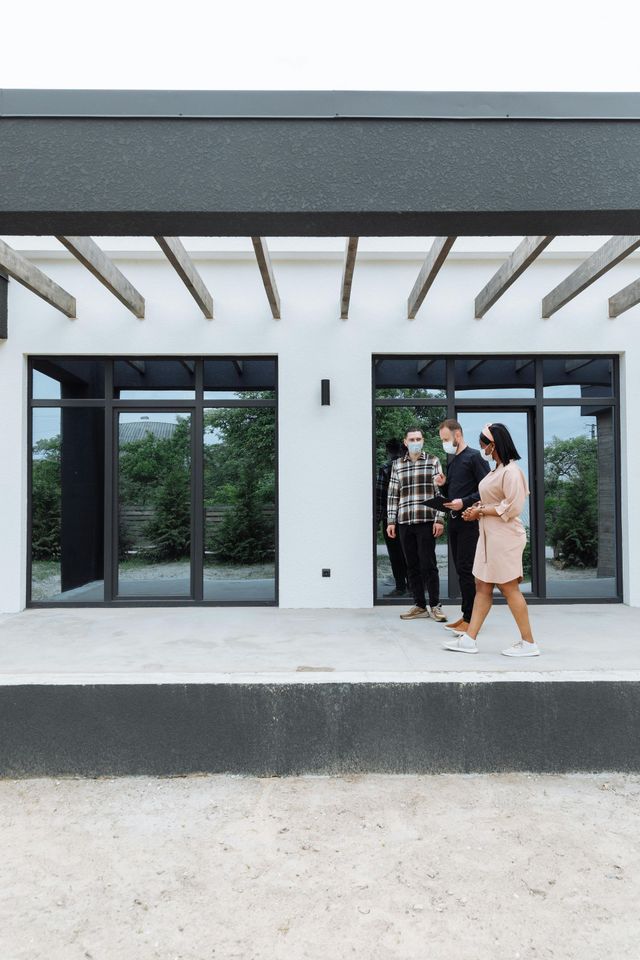 A group of people wearing face masks are standing outside of a house.