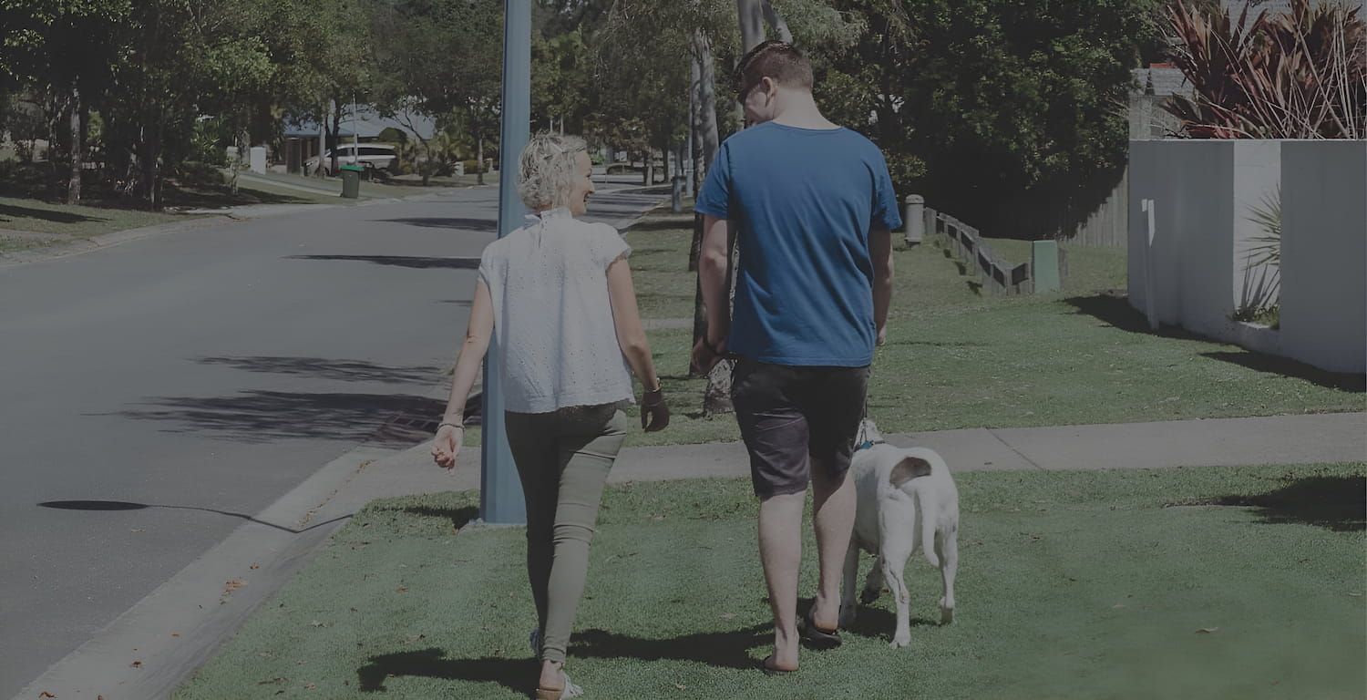 A Man And A Woman Are Walking A Dog Down A Sidewalk — Tailored Support Services Pty Ltd In Maroochydore, QLD