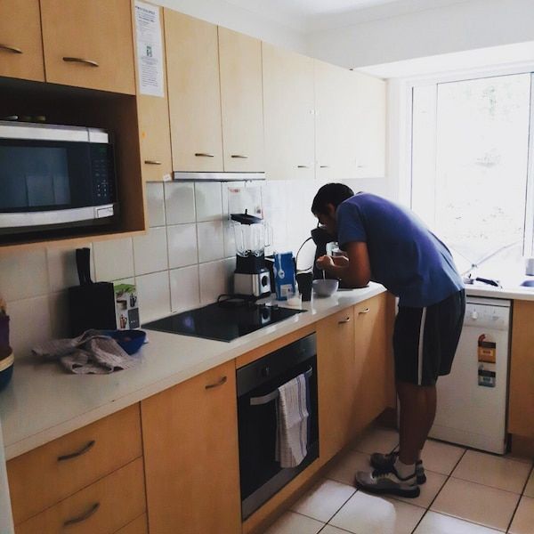 A Man In A Blue Shirt Is Pouring Something Into A Cup In A Kitchen — Tailored Support Services Pty Ltd
 In Buderim, QLD