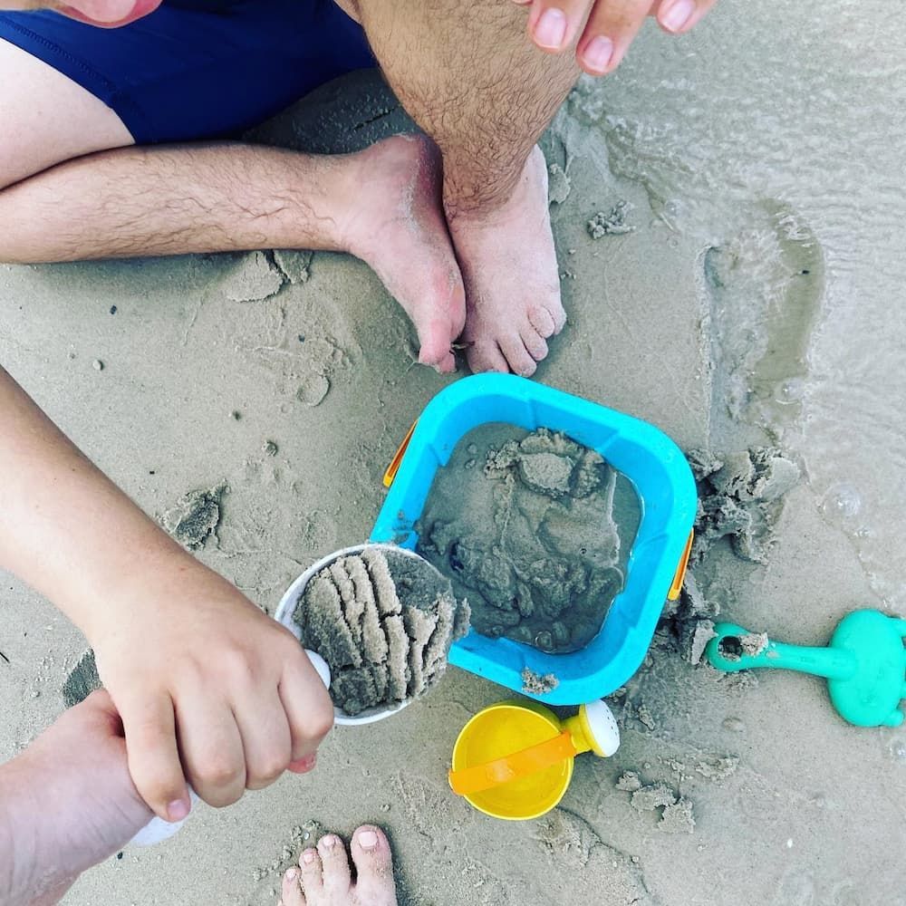 A Man And Two Children Are Playing In The Sand On The Beach — Tailored Support Services Pty Ltd In Sippy Downs, QLD