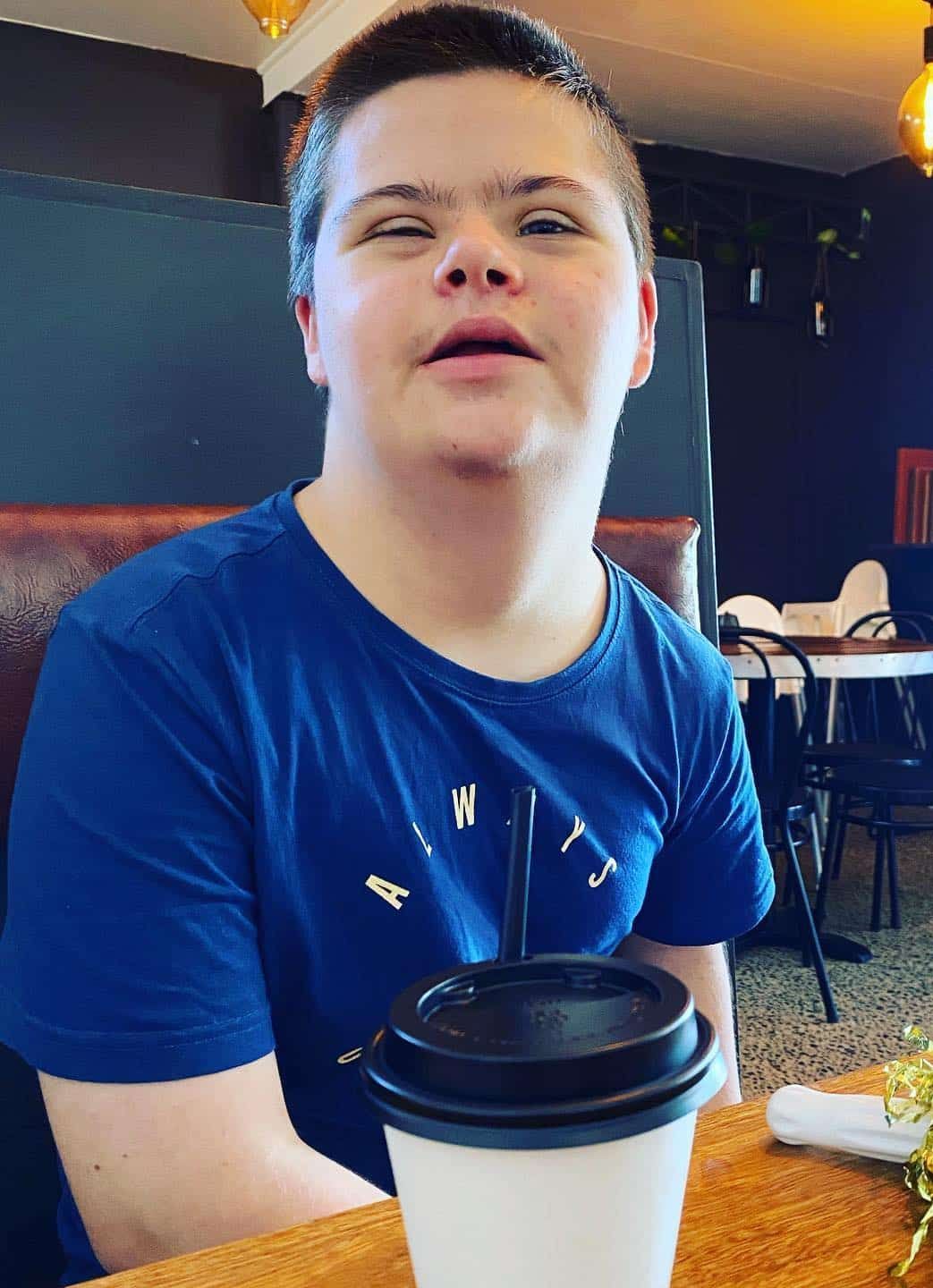 A Young Boy Is Sitting At A Table With A Cup Of Coffee — Tailored Support Services Pty Ltd In Maroochydore, QLD