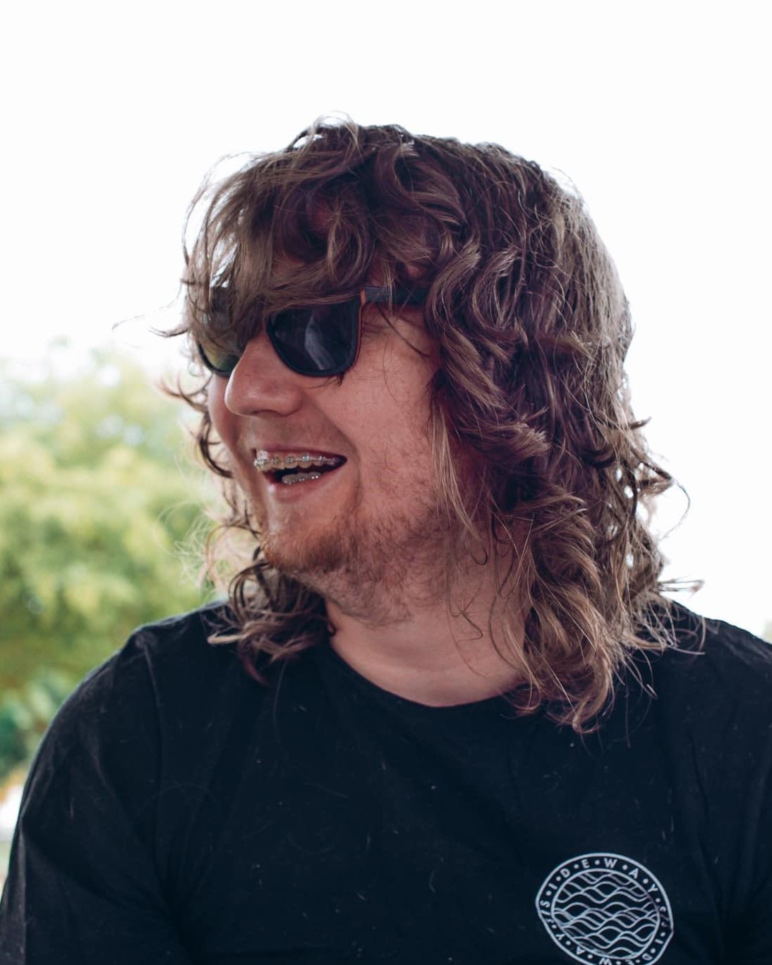 A Man With Long Curly Hair And Sunglasses Is Smiling — Tailored Support Services Pty Ltd In Maroochydore, QLD