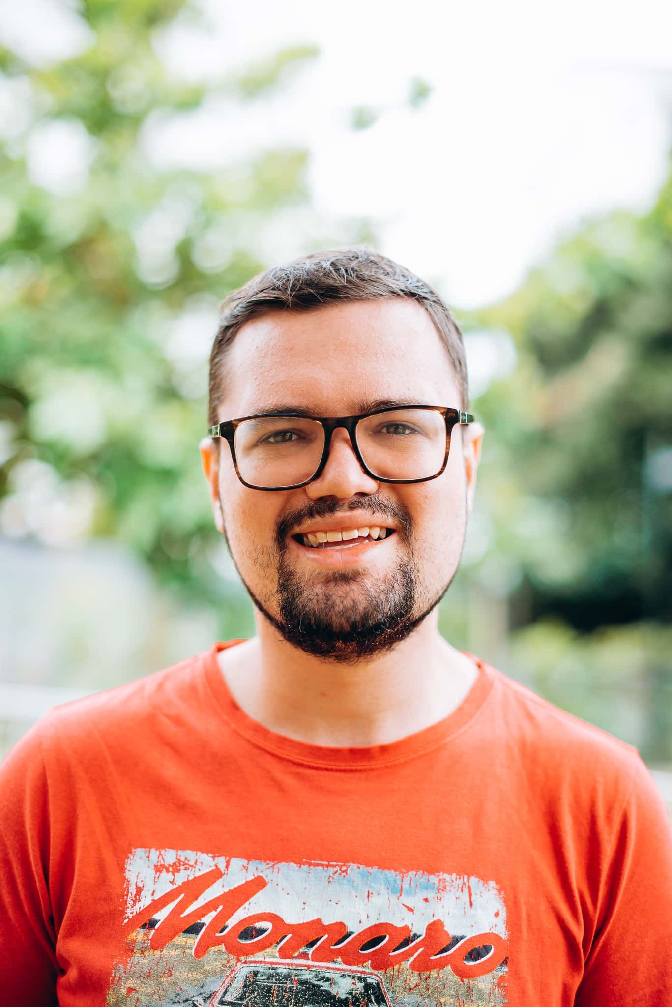 A Man With A Beard And Glasses Is Wearing A Red Shirt And Smiling — Tailored Support Services Pty Ltd In Maroochydore, QLD