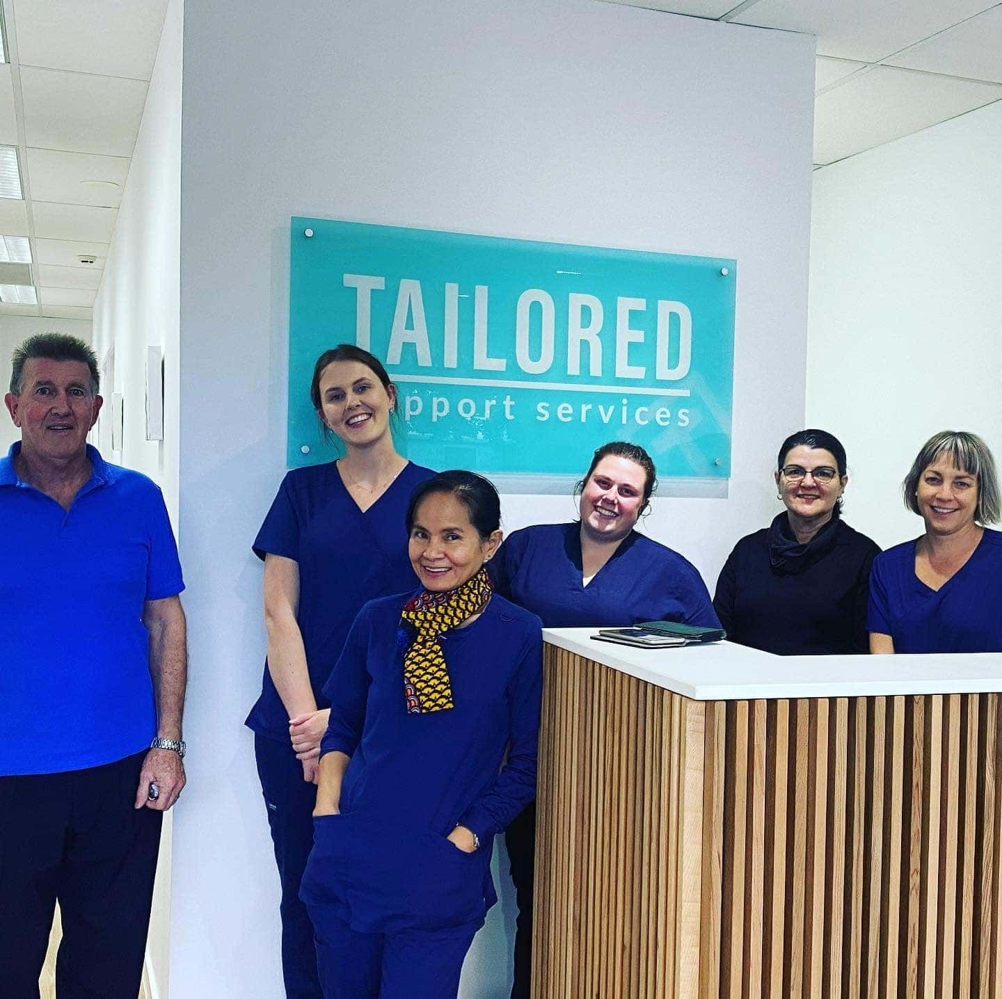 A Group Of People Posing In Front Of A Sign Says Tailored Support Services — Tailored Support Services Pty Ltd In Maroochydore, QLD