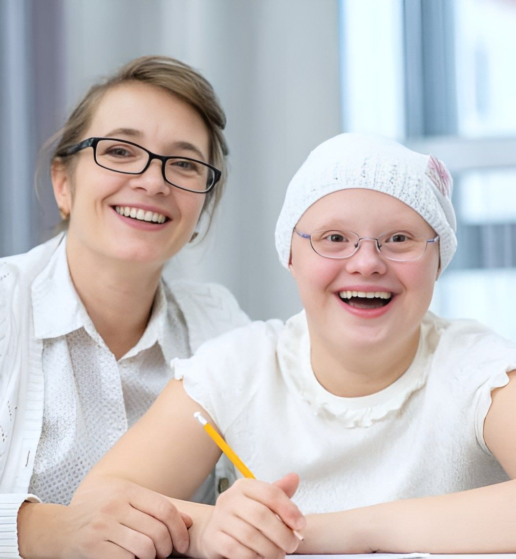 A Woman And A Girl With Down Syndrome Are Smiling At The Camera — Tailored Support Services Pty Ltd In Caloundra, QLD