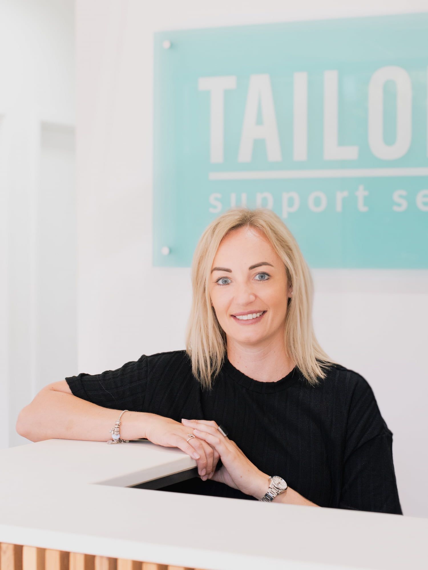 A Woman Leaning On A Counter In Front Of A Sign That Says Tailors Support — Tailored Support Services Pty Ltd In Maroochydore, QLD