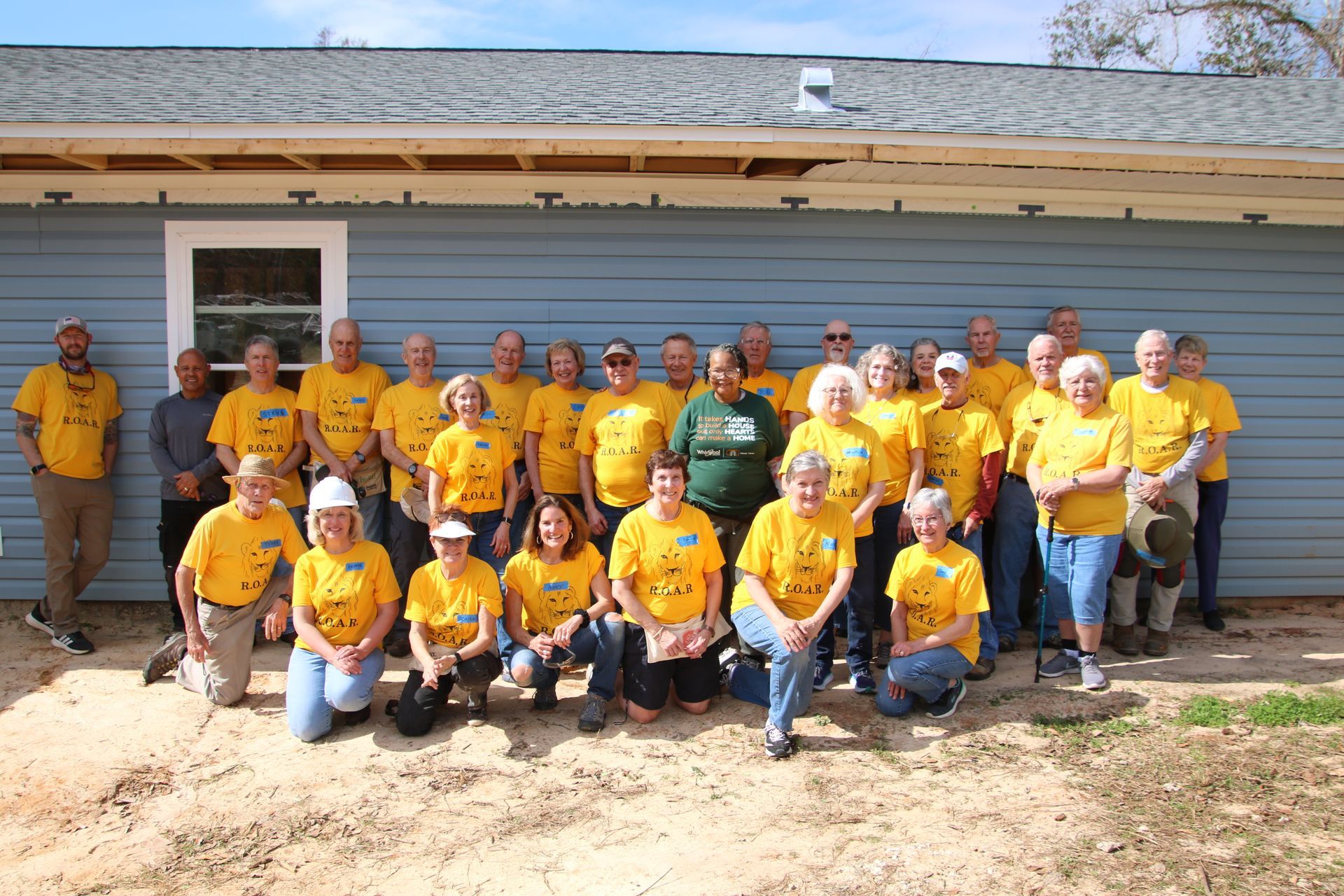 A group of people standing in front of a house wearing yellow shirts