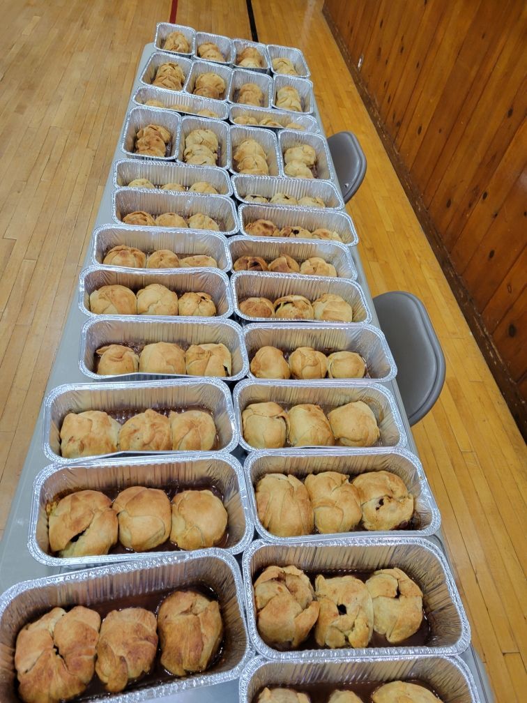 A table full of aluminum foil containers filled with apple dumplings
