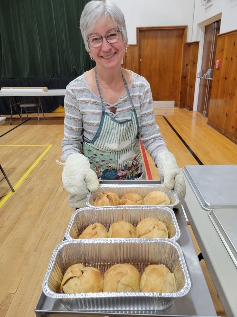 A woman is smiling while holding a tray of apple dumplings.