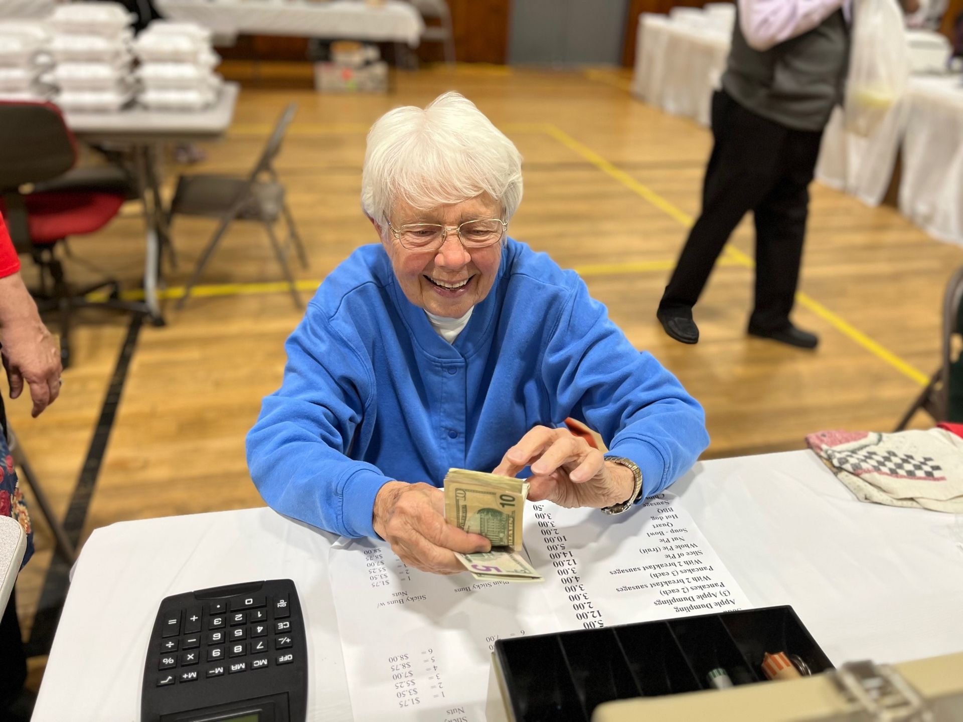 A woman in a blue sweater is sitting at a table holding a dollar bill