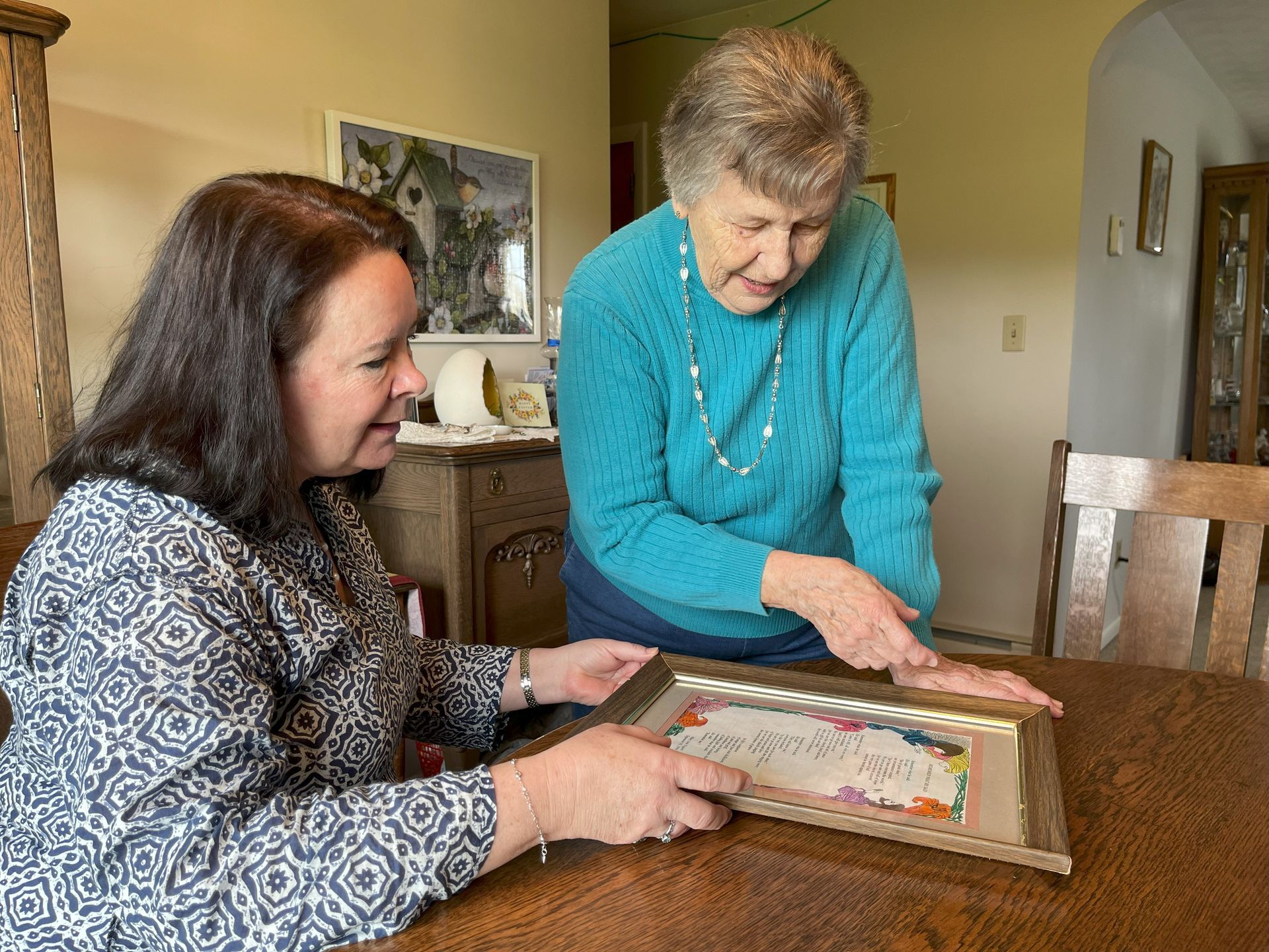Two women sit at a table looking at a framed picture