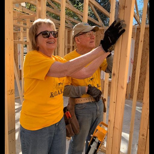 Two volunteers wearing yellow shirts and gloves, building a house frame.