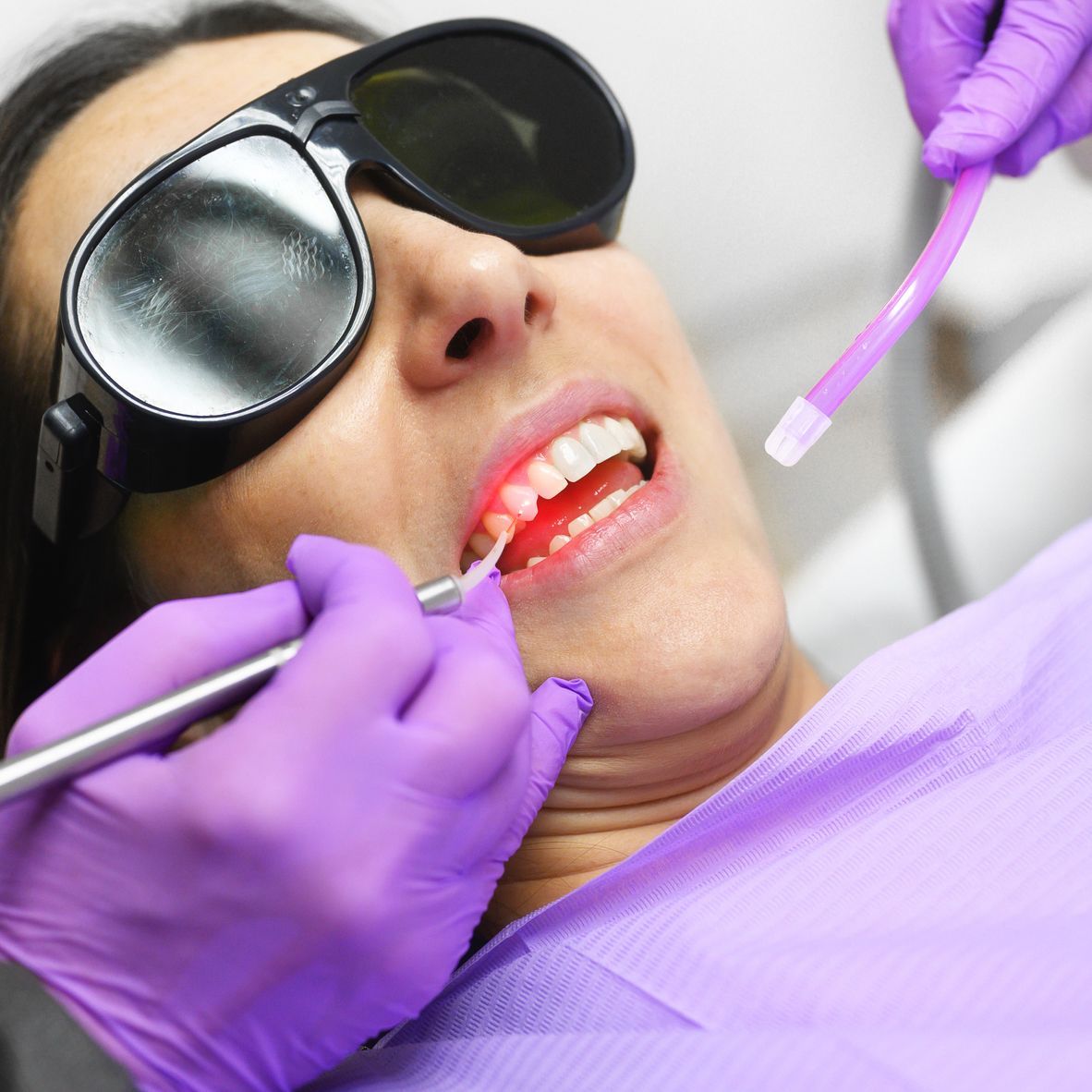 A woman wearing sunglasses is getting her teeth examined by a dentist