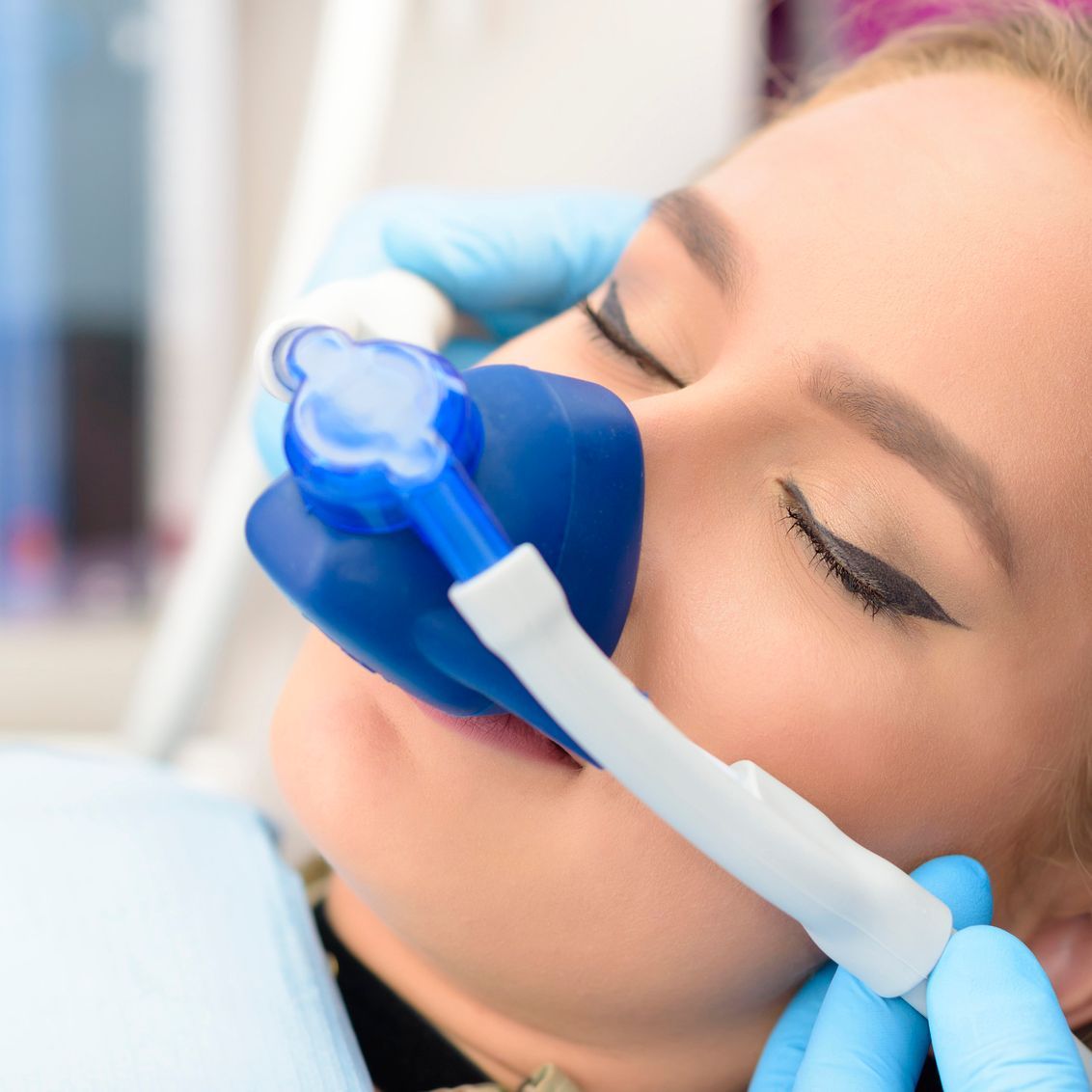 A woman is laying in a dental chair with an oxygen mask on her face.